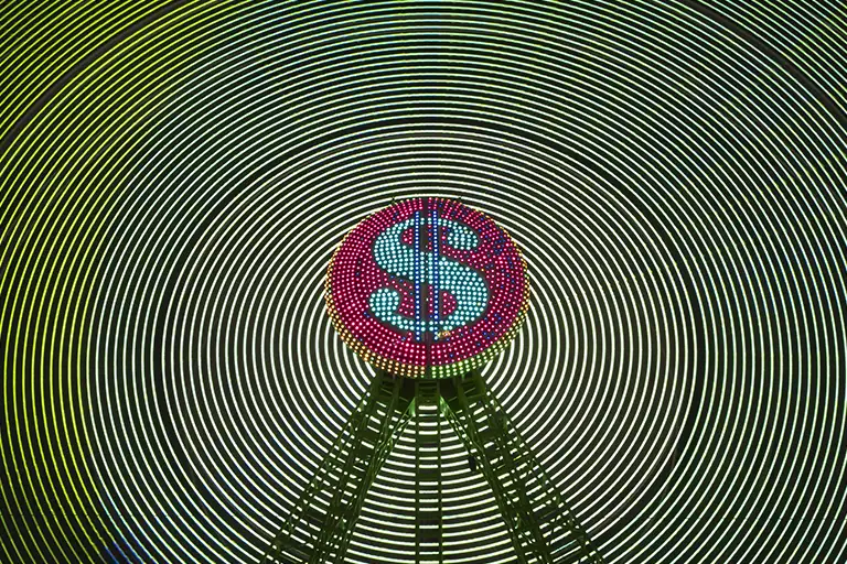 A picture of a ferris wheel with a dollor sign in lights representing how sync licensing generates income from three separate streams: upfront fees (one-time payment), PRS performance royalties (ongoing broadcast payments), and PPL neighboring rights (ongoing public performance)