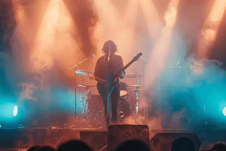 Atmospheric live concert viewed from the crowd, band on stage through lights and smoke, illustrating the traction that music management is built to amplify rather than create.