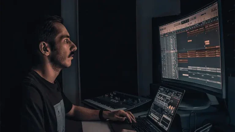Independent musician in a dark home studio, balancing music production and streaming analytics across laptop and screen, illustrating the data paradox at the heart of music industry.