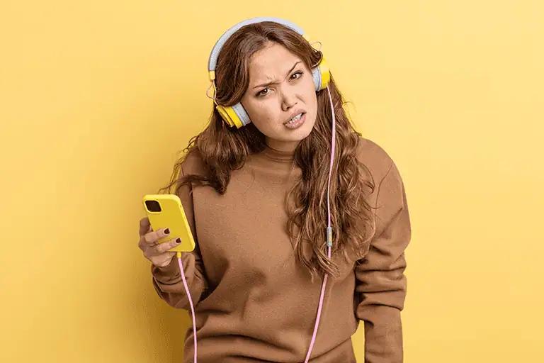 A woman wearing headphones looks puzzled at her smartphone, much like listeners weighing up what they think of AI music in their streaming feeds